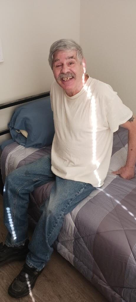 Jeff sitting on his newly made bed at Central Park Place, with sheets, comforter, and pillow from donors